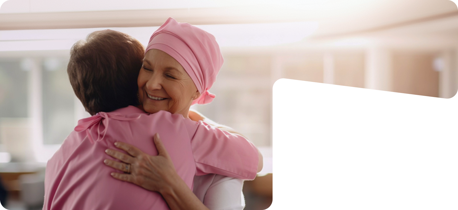 Two women embracing, one wearing a pink headscarf, in support of breast cancer awareness